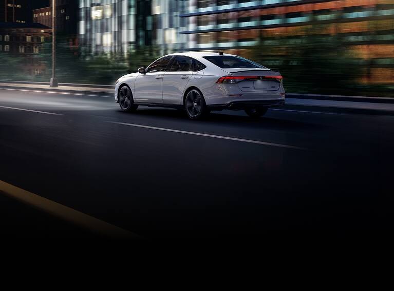 2026 Honda Accord 3/4 rear view in Platinum White Pearl driving in the city at night. 2026 Honda Accord 3/4 rear view in Platinum White Pearl driving in the city at night.