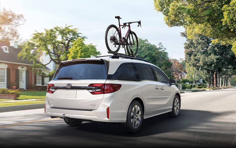 2027 Honda Odyssey Elite in Platinum White Pearl back driving through a sunny residential neighborhood (Minivan).