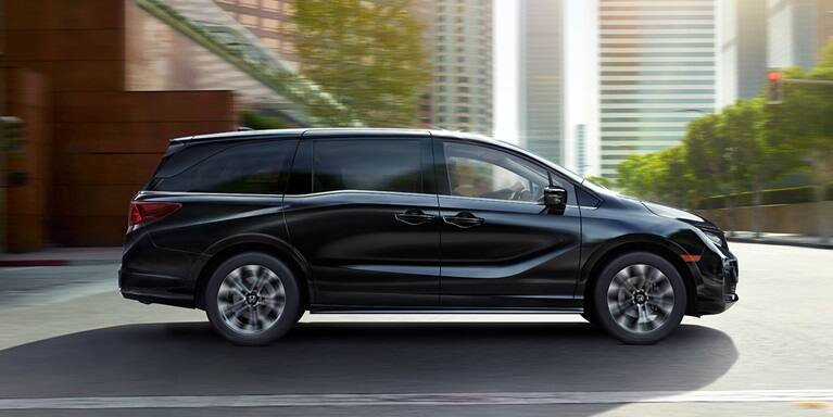 2027 Odyssey Elite family van in Crystal Black Pearl driving on a city street (Minivan).